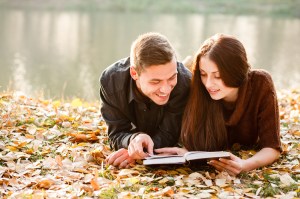 young male and female lying down near lake reading book